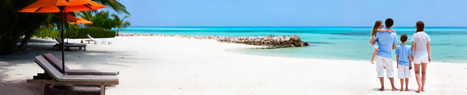 Family walking hand in hand on a white beach beside turquoise water