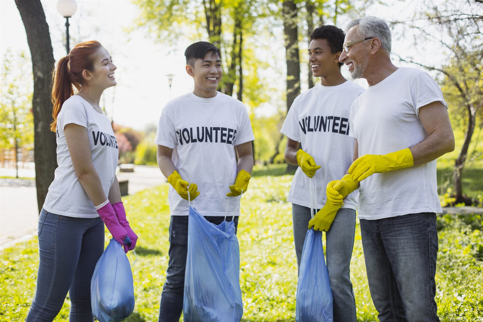 Smiling volunteers in matching shirts holding gloves and trash bags in a park