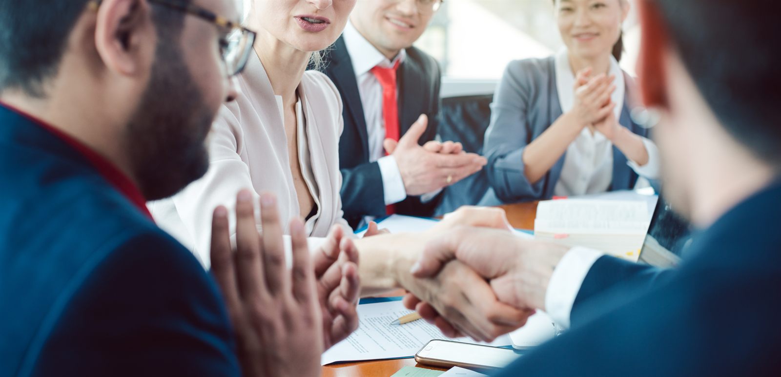 Colleagues applauding and shaking hands across a meeting table